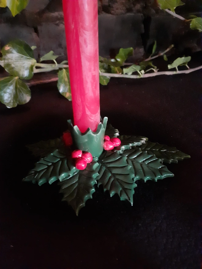 Close-up of a red taper candle in a green holly holder, showing the glossy leaf details and bright red berries.