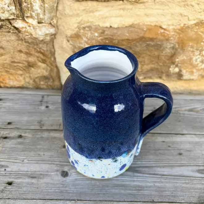 Shoreline Medium Jug, a colourful jug sitting on a wooden surface against a brick wall backdrop. 