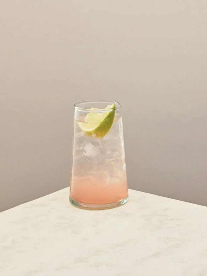 Highball Glasses (Set Of 1 Or 4), a highball glass sitting on a plain counter top against a white backdrop. It is filled with a soft drink. 