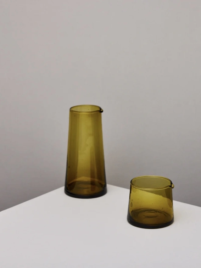 Tall Jug, a tall amber glass jug sitting on a plain counter top against a white backdrop. It is accompanied by a smaller amber glass