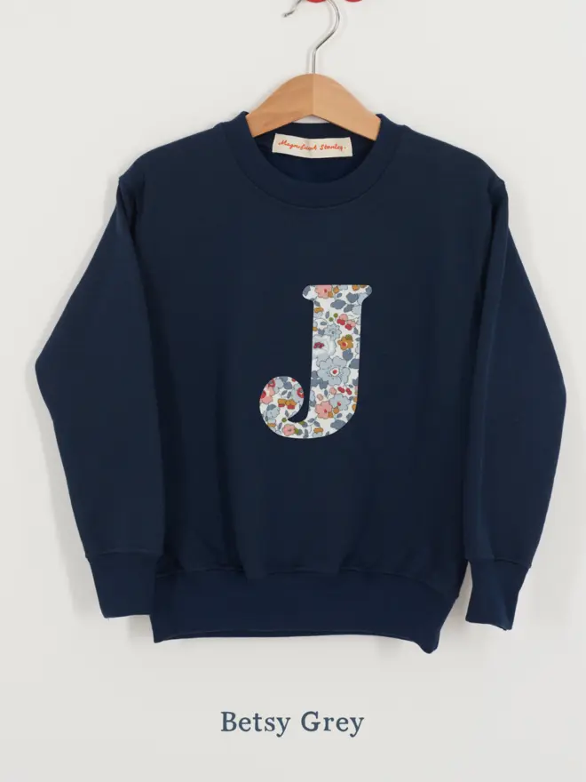 a navy kids sweatshirt with the initial J personalised in floral liberty print on the front