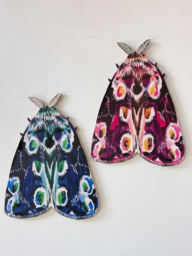 large wooden moth wall decoration. large pink and blue wooden moth decorations hung on plain white wall.