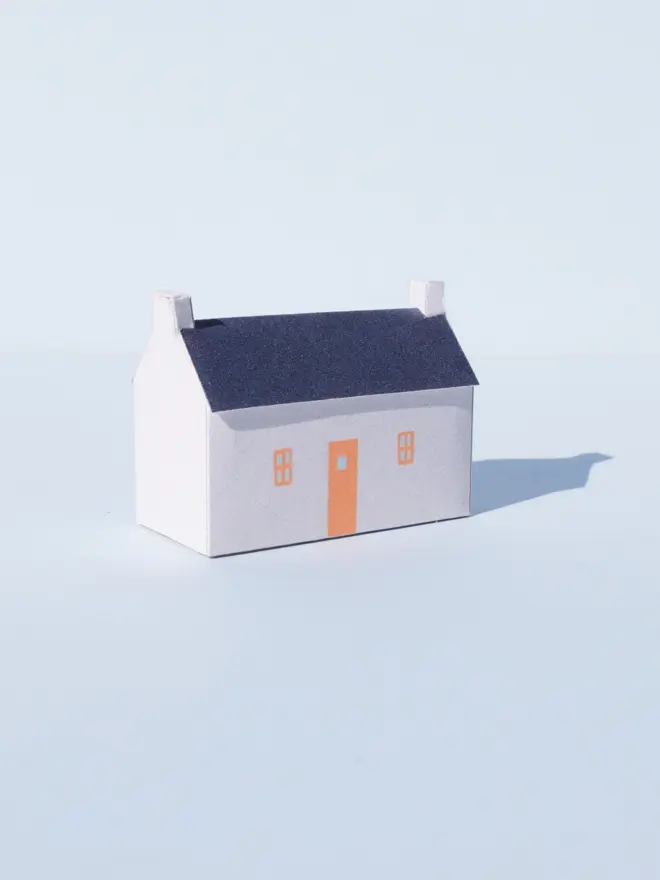 Paper house with a white facade and orange doors and windows