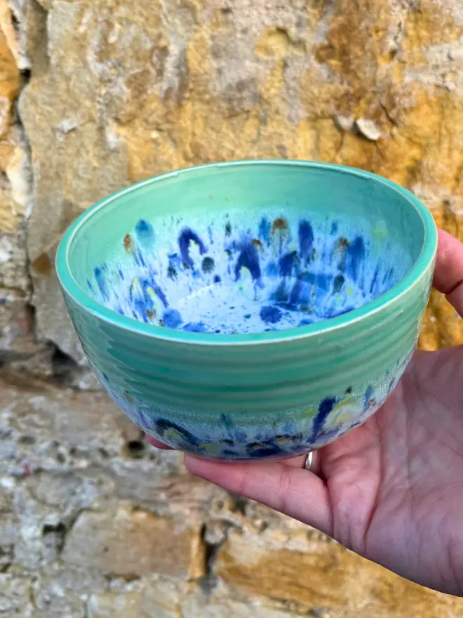 Shoreline Small Bowl, a colourful bowl held in front of a brick wall. 