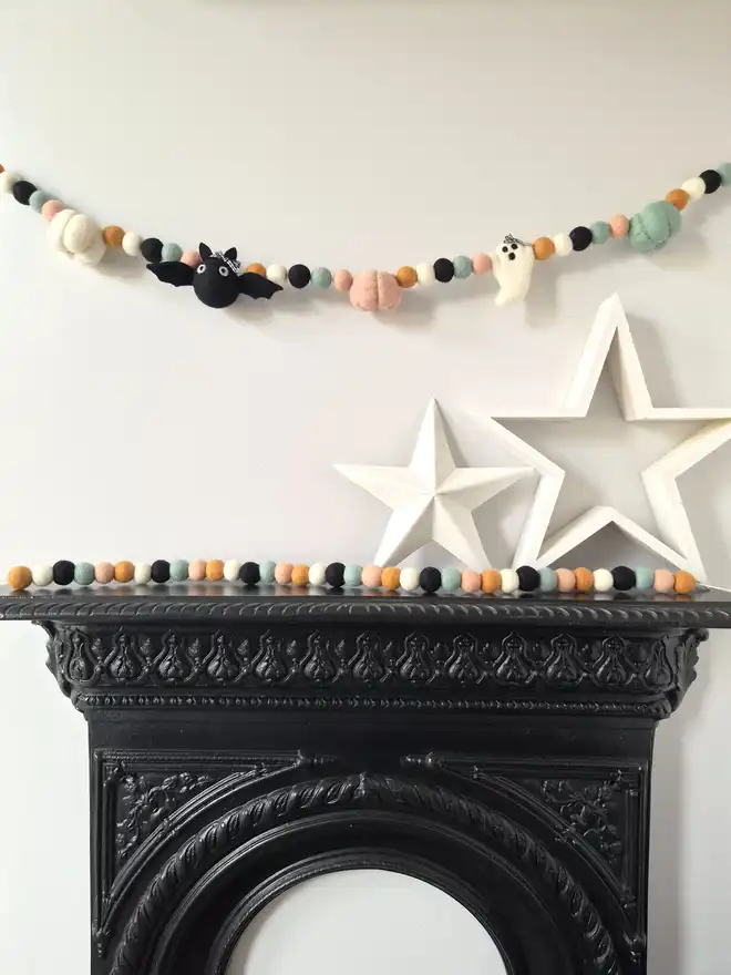 Pastel Halloween garland with a bat, ghost and pumpkins, hung above a firplace.