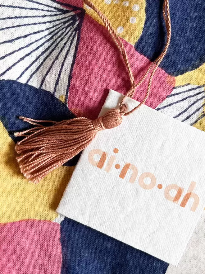 Detail of recycled swing tag with ainoah logo printed and dusty pink tassel on a hanging loop 