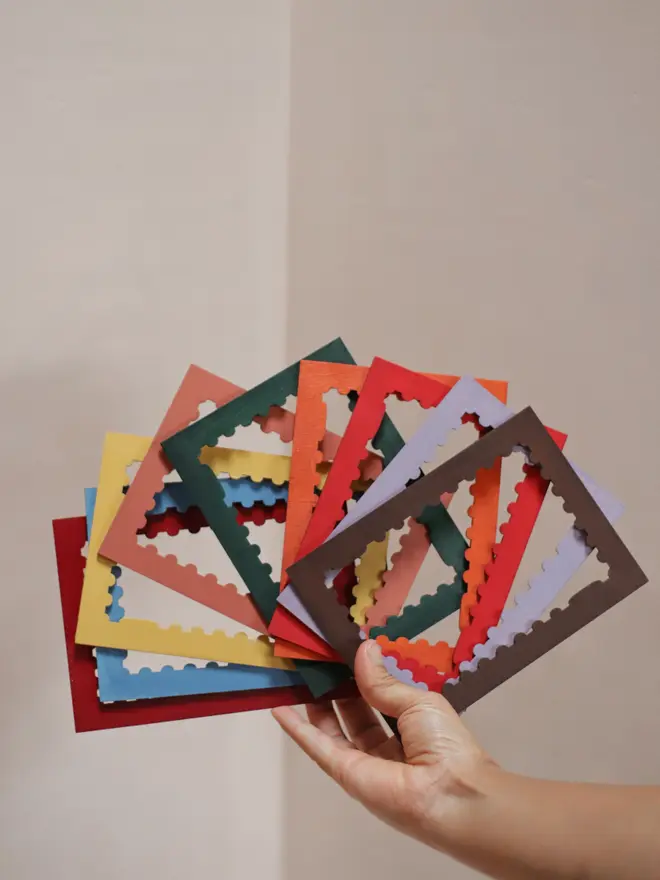 selection of multicoloured stamp-shaped picture frame mounts, held in one hand