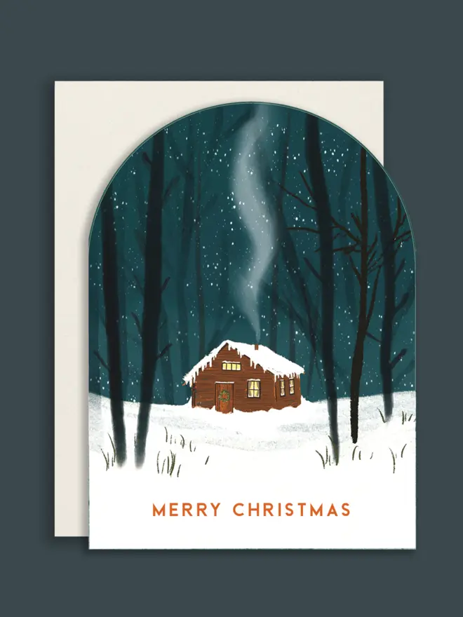 Arched shape Christmas card with white envelope, with an illustrated cabin scene in the snowl