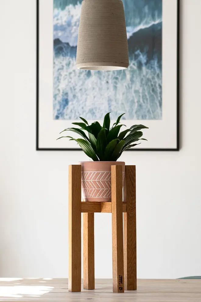 Oak Pot Stand, a wooden oak pot stand sitting in a living room on a wooden surface. It is accompanied b a picture and a light. 