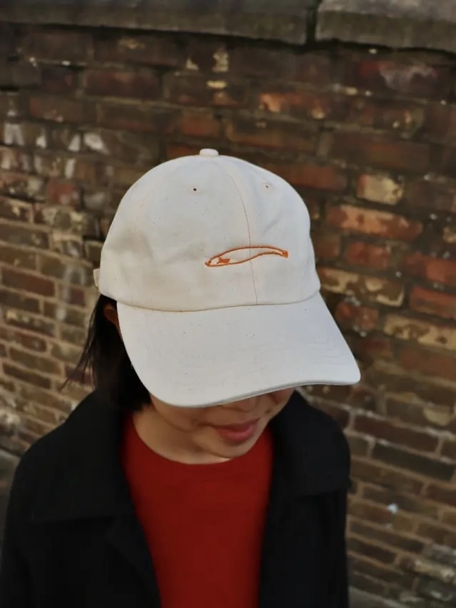 Omiyage Collection, a person wearing a cap against a brick wall. 