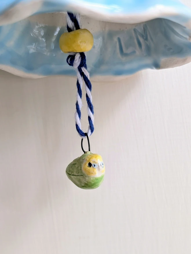 white budgie bell in ceramic with a tiny yellow and green budgie shown in close up of the bird