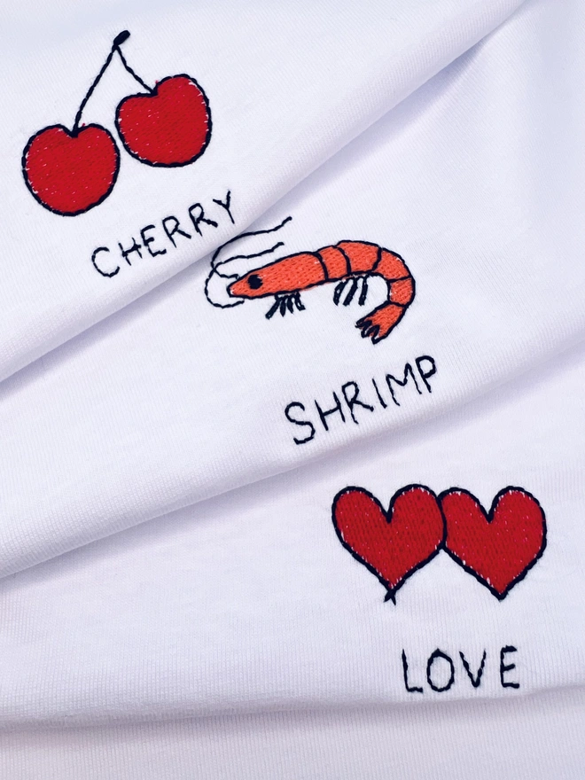     Close-up showing embroidered cherry, shrimp and heart motifs on white T-shirts