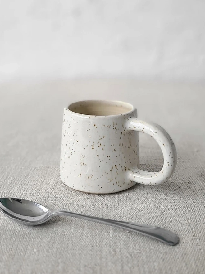 Classic Ceramic Espresso Mug, a colourful ceramic espresso mug sitting on a plain surface against a white backdrop. It is accompanied by a spoon. 