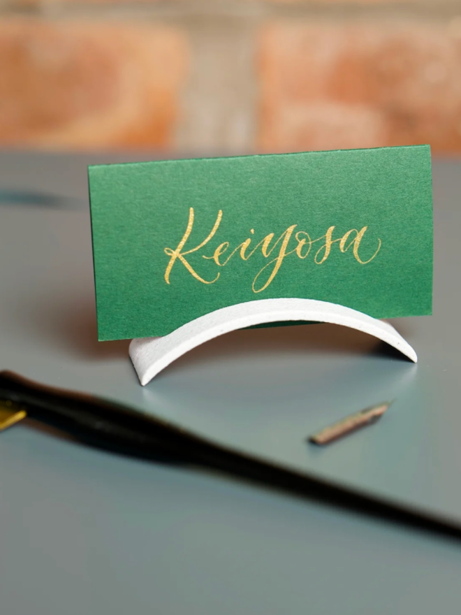 Hue Arch Place Card and Card Holder. The card is shown in the holder, which is a pleasing arch shape, with a pen next to them.