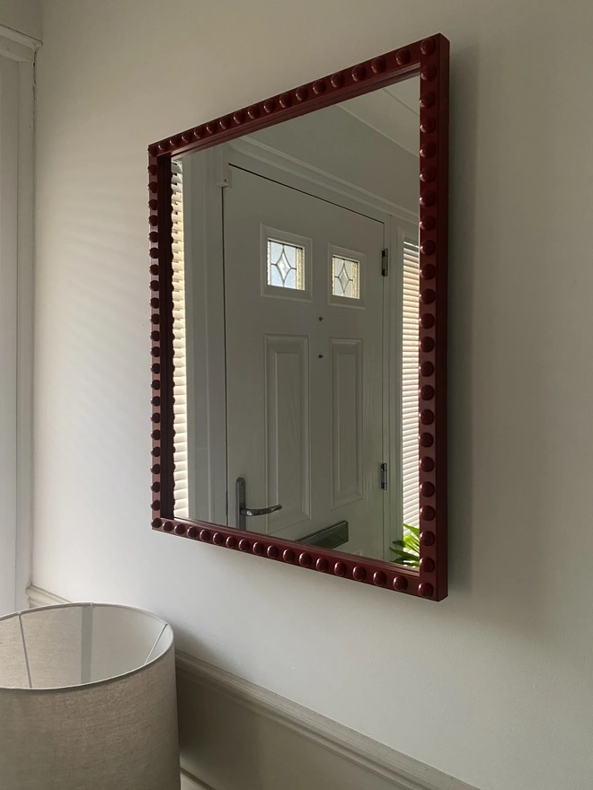 A side angle of a burgundy bobbin mirror hung in a hallway