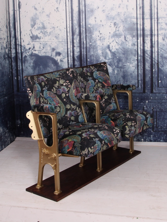 Side view of a set of two vintage cinema seats, seats are open and the set is against a blue marbled wall