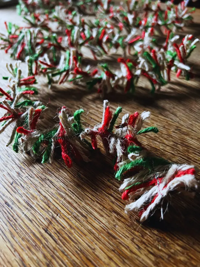 Close up of red, white and green Candy Cane jute string tinsel AKA Strinsel laid out randomly on an oak table