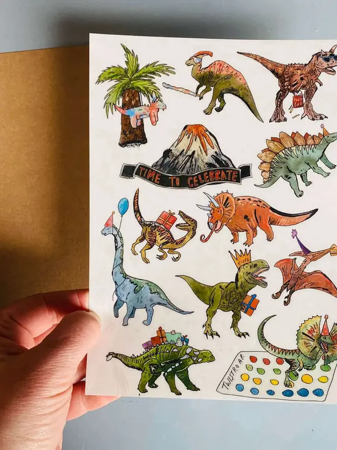 Dinosaur & Fantasy Temporary Tattoos, a hand holds a brown kraft paper booklet titled "DINOSAUR TATTOOS" next to a tattoo sheet with colorful dinosaur illustrations.