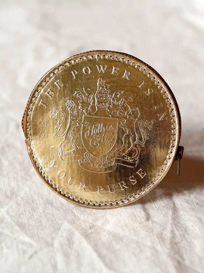 A gold leather coin purse with a metal zip placed on a white tablcloth 