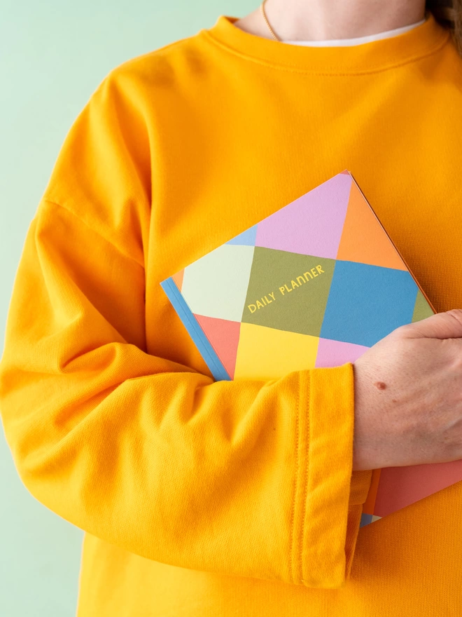 Woman in orange jumper holds colourful harlequin design Raspberry Blossom daily planner