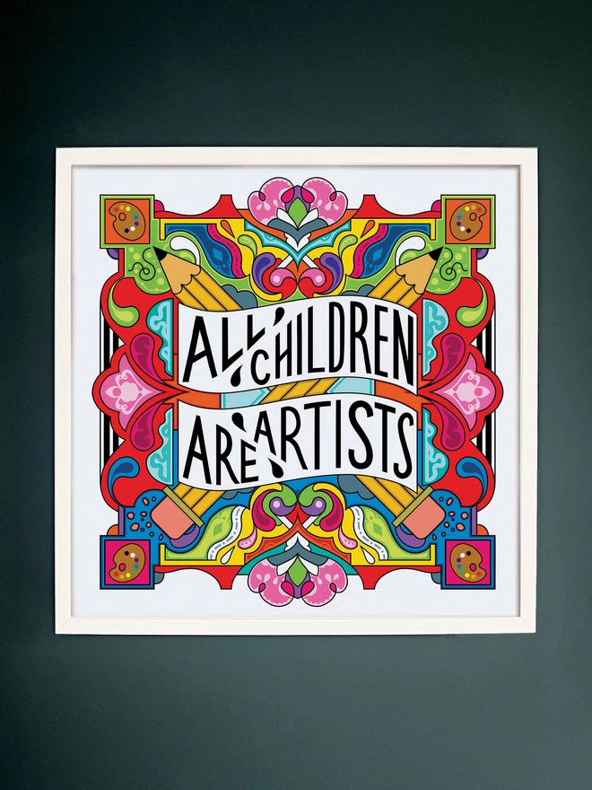 A white square frame surrounds the print, which has the words All Children are Artist at the centre of this multi-coloured vibrant illustration which includes a cross of pencils, and artists palettes the corners. It is hung on a dark grey wall.