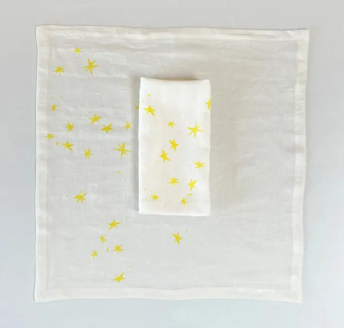 Stars Napkins In White (Set of 4). White cloth napkins with scattered yellow star prints, placed on a white table cloth. 
