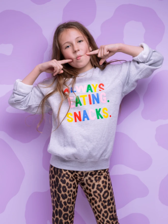 Child wearing a grey sweatshirt with Always Eating Snacks slogan