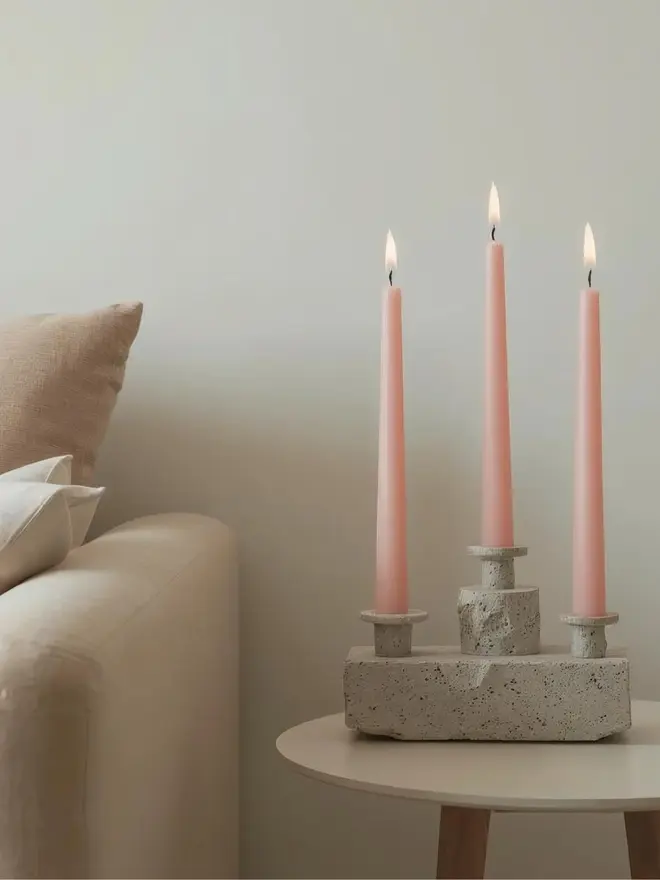 three blush pink dinner candles in a concrete candle holder on a side table