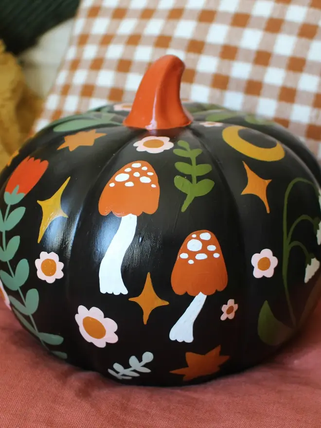 hand-painted folk art ceramic pumpkin. a black ceramic pumpkin painted with mushrooms and flowers.