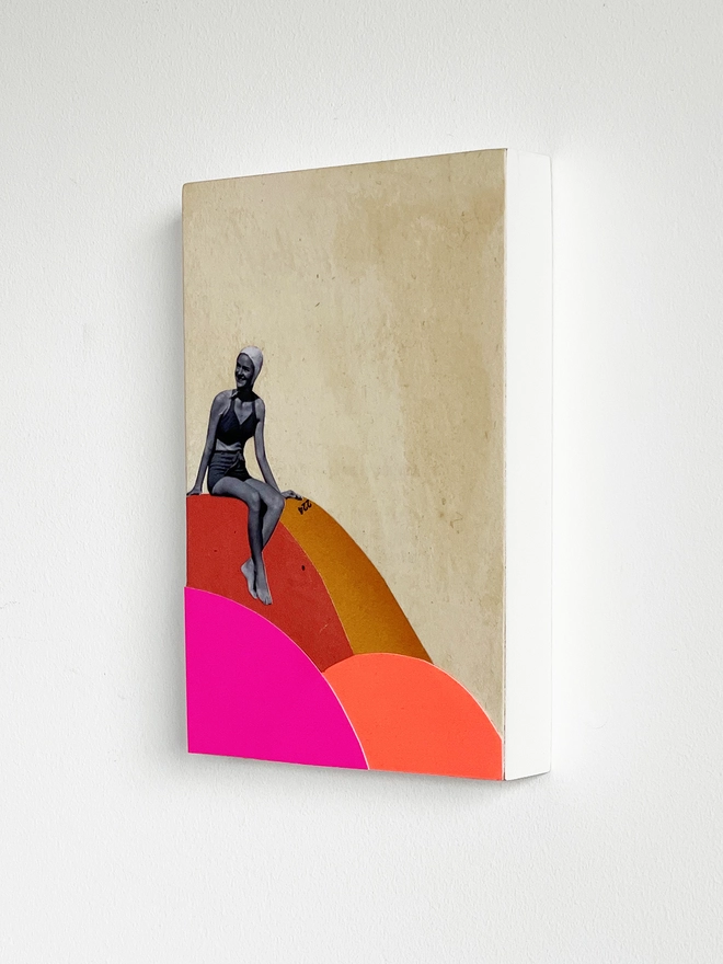 A brightly coloured artwork made with a mix of neon pink and orange card and vintage papers. It is a female portrait of a swimmer who is about to dive off the colourful rocks into the sea.