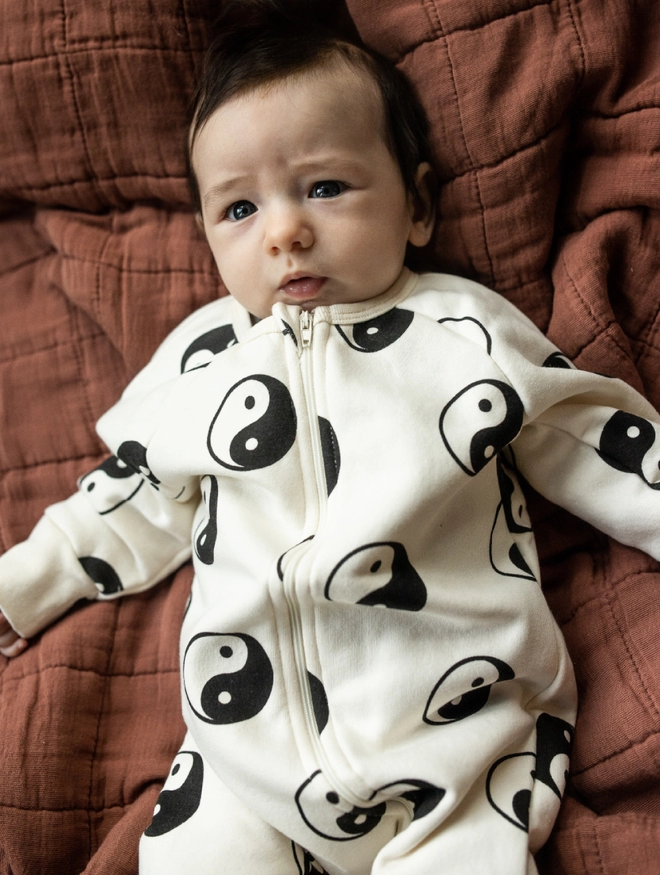 Another Fox Yin Yang Baby Sleepsuit seen on a baby lying on brown bedding.