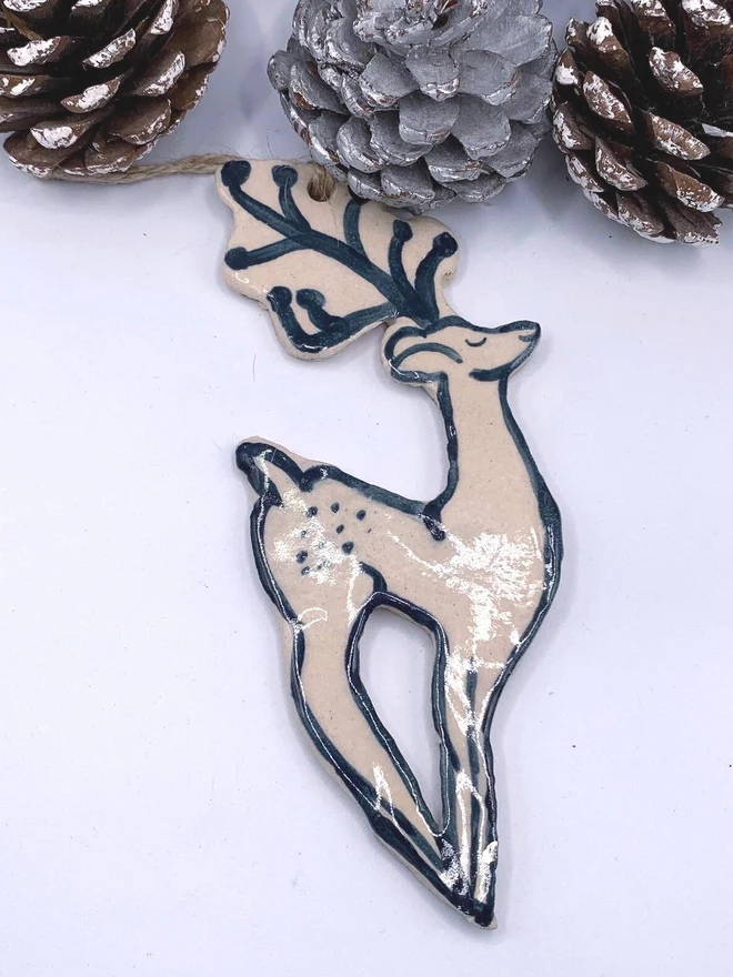 Handmade Ceramic Reindeer Ornament Scandinavian Folk Decor, a colourful reindeer decoration sitting on a plain surface joined by some acorns. 