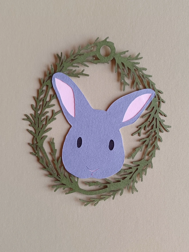 Black Bunny Easter Tree Decoration. Dark grey bunny face with black eyes and pale pink ears inside olive green foliage wreath oval