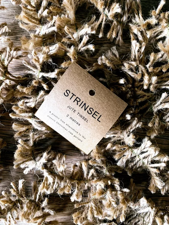 A tumble of undyed jute string tinsel AKA Strinsel packaged in a kraft card label on an oak table