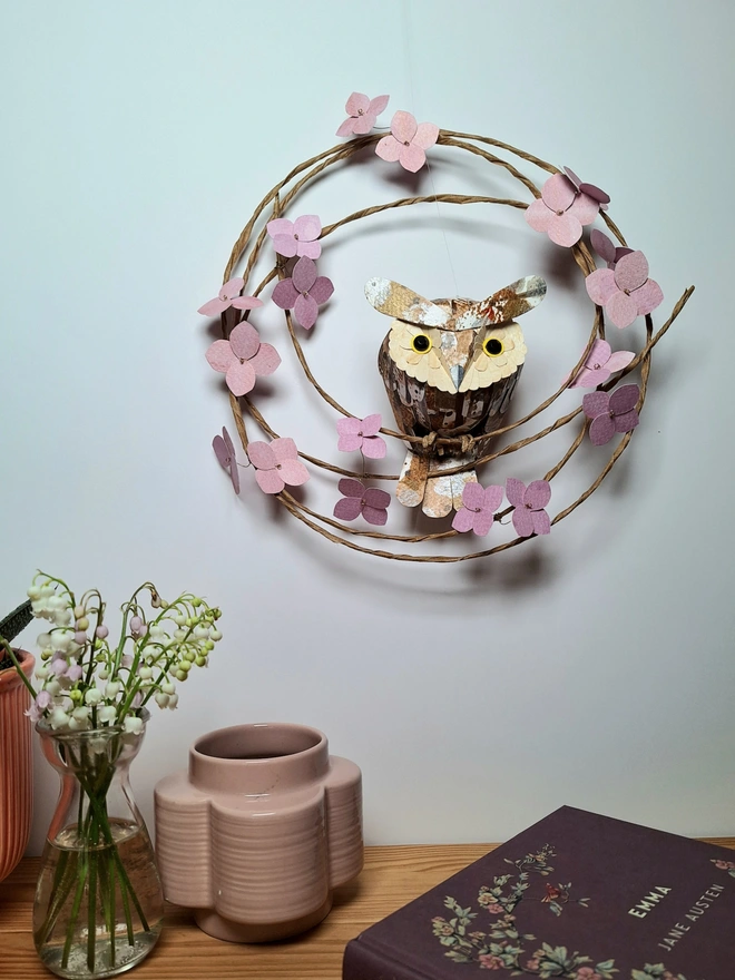 Handmade paper sculpture of a baby long eared owl, perched on a wreath of pink hydrangea blossoms
