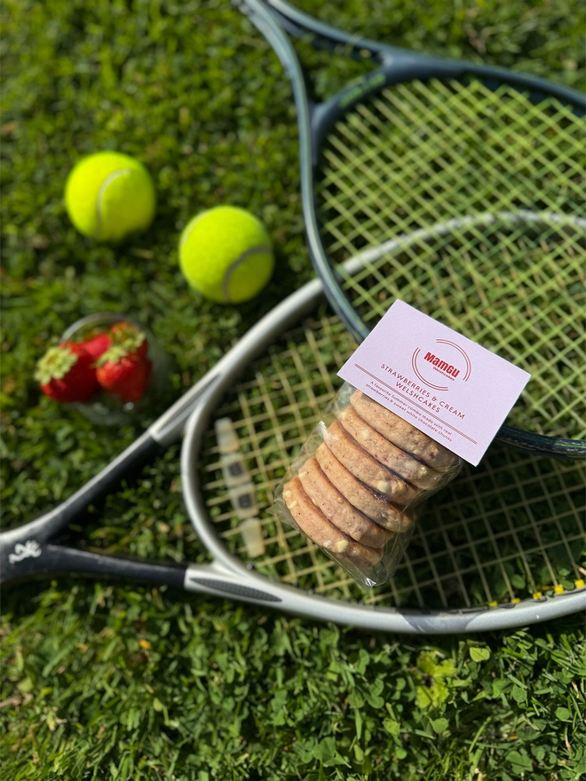 6 pack of strawberries and cream welsh cakes on a tennis racket, with balls, and strawberries on the grass.