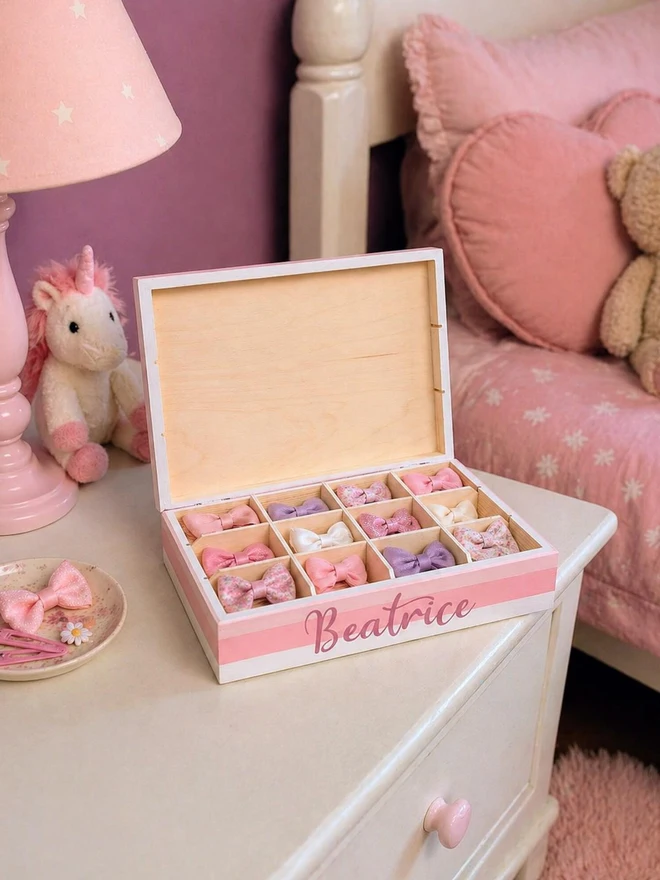 personalised rainbow kids' jewellery box. a pink sectioned box containing a child's hair ties.