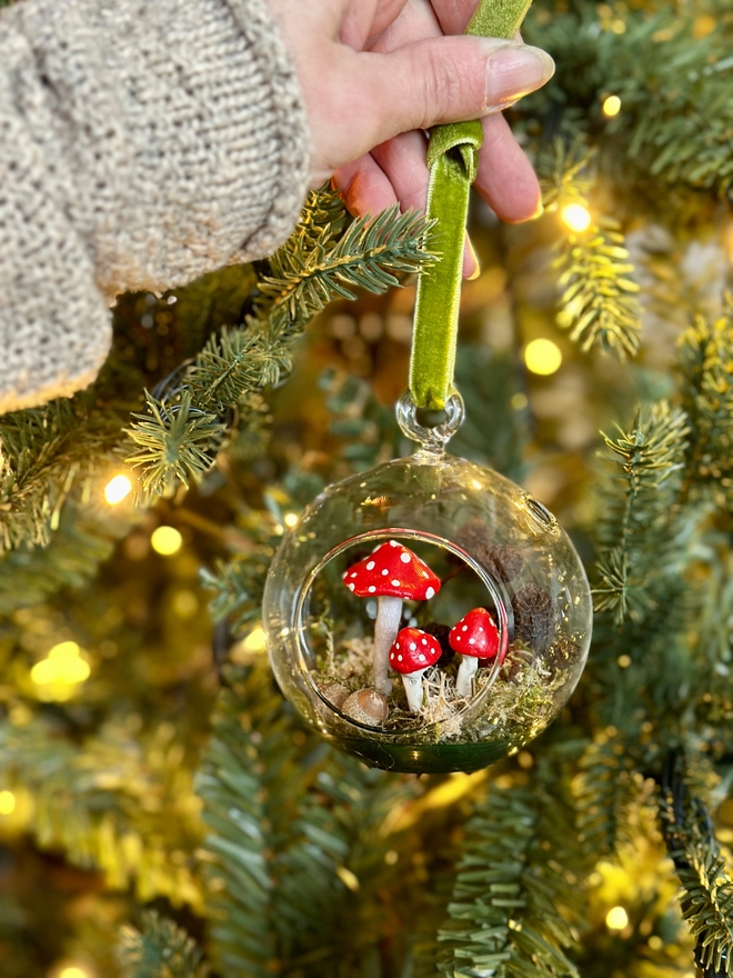 Glass Bauble filled with handmade toadstools and alder cones sbeing attached to a Christmas tree