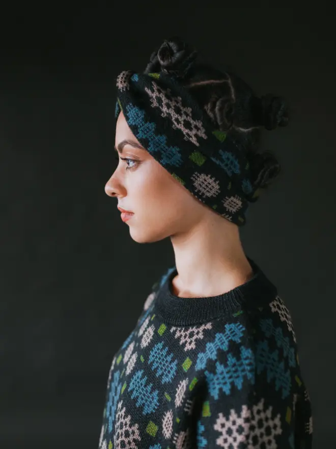 Model wearing pieces from MABLI's 'Carthen' collection, featuring the Carthen Wrap in the vibrant 'Emeralds' colour-way. The design showcases bold, colourful patterns inspired by traditional Welsh blanket tapestry.