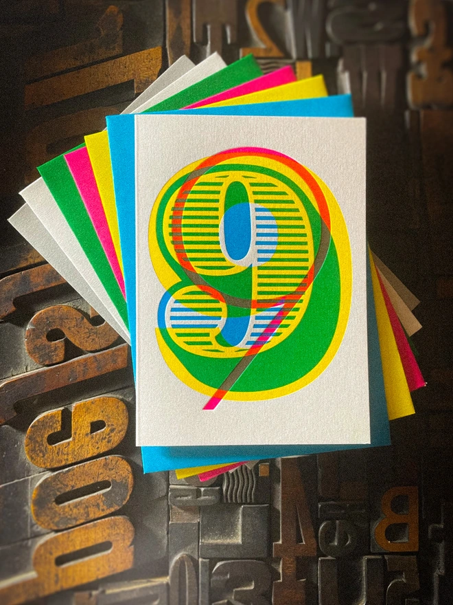 Handmade letterpress 9th birthday card featuring bold overlapping numerals printed in vibrant fluorescent cyan, magenta and yellow inks. Each card is individually hand printed using traditional letterpress techniques on luxury paper stock, creating a beautifully tactile finish with a deep impression and rich layered colours inspired by the CMYK printing process. Printed on a traditional letterpress from 1915. A wonderful artisan printed birthday card.