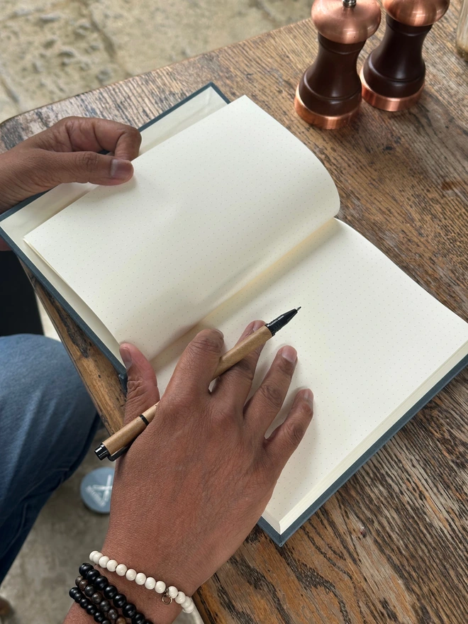 An open notebook filled with dotted bullet journal pages is held by a man who also holds a pen.