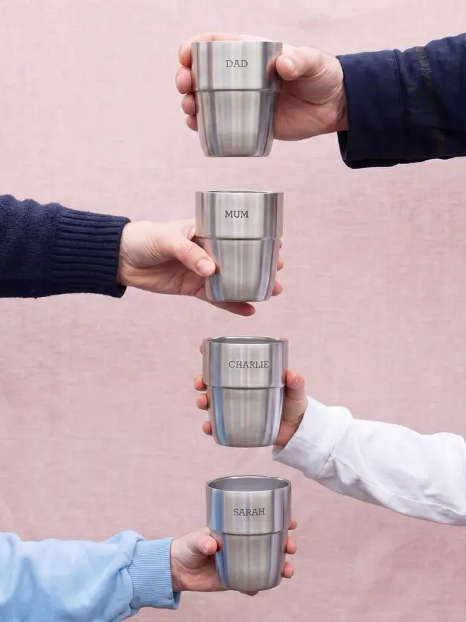 'expedition' stainless steel stacking cups set. four personalised stainless steel cups, held in hands in a vertical formation against a pink background.