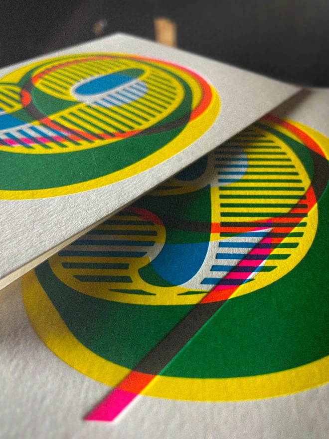 Detail of handmade letterpress 9th birthday card featuring bold overlapping numerals printed in vibrant fluorescent cyan, magenta and yellow inks. Each card is individually hand printed using traditional letterpress techniques on luxury paper stock, creating a beautifully tactile finish with a deep impression and rich layered colours inspired by the CMYK printing process. Printed on a traditional letterpress from 1915. A wonderful artisan printed birthday card.