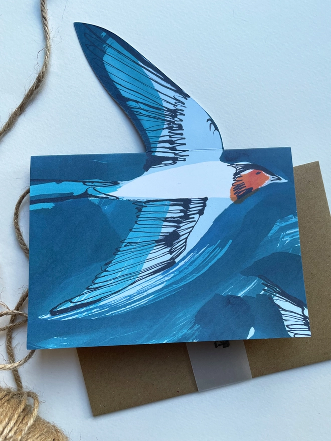 Esther Kent illustrated greeting card showing inky blue swallow illustration on a teal background. The swallow's wing pops u.