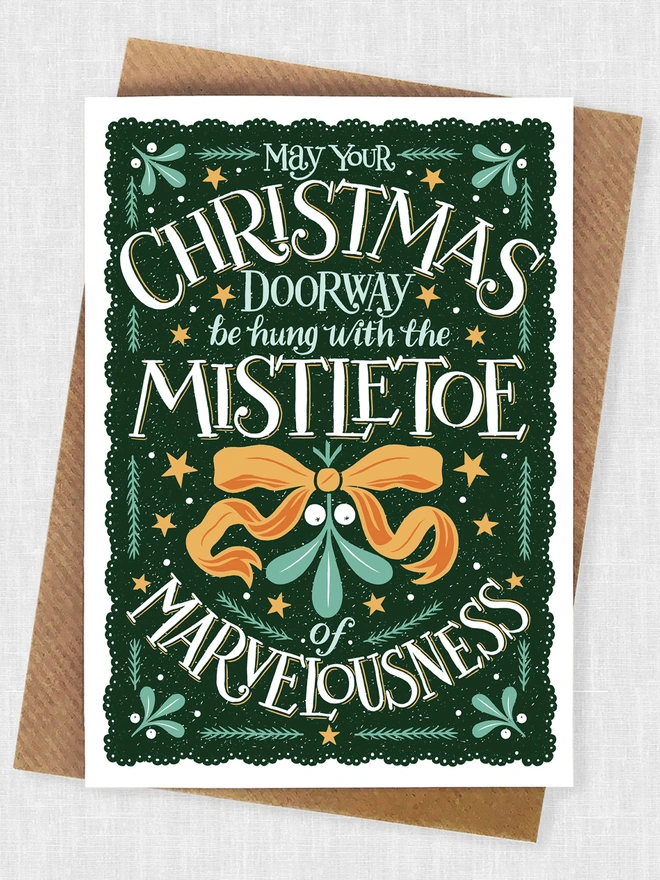 christmas mistletoe card on a dark green background with orange ribbon