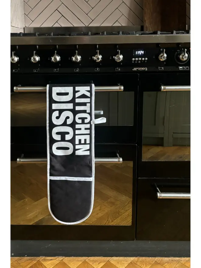 Black oven glove with white text that says KITCHEN DISCO hanging on oven door