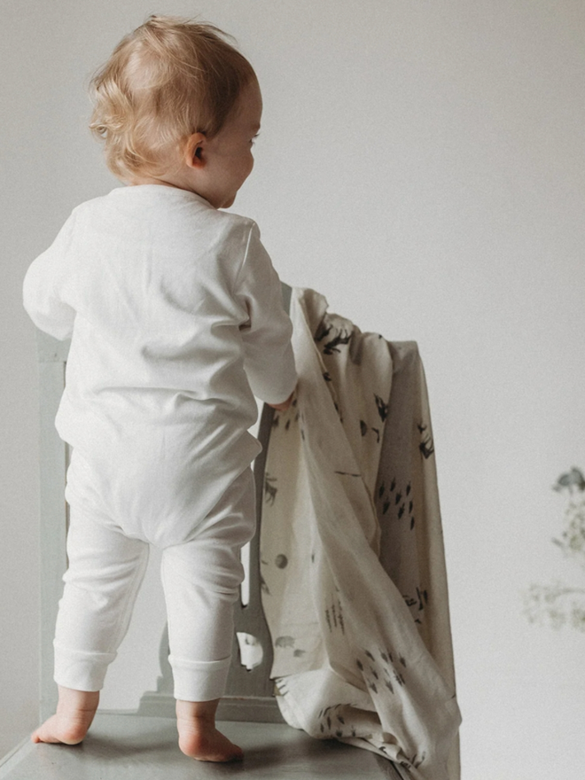 The Way Home Muslin. A baby with a muslin, with a wildlife monochromatic pattern.