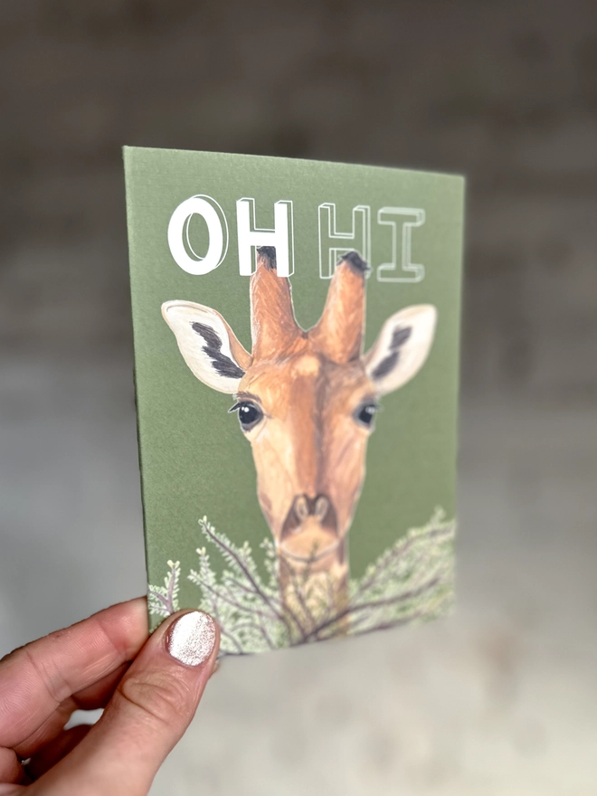  a green greetings card featuring an illustration of a giraffe peering over a bush
