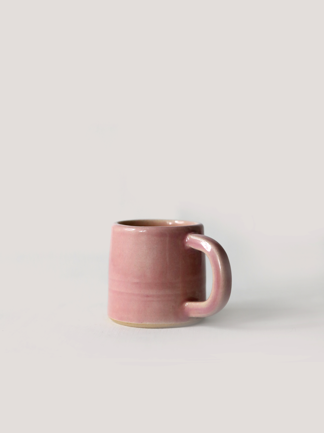 A handmade ceramic espresso mug in blush pink glaze, with a chunky loop handle, photographed against a plain light grey background