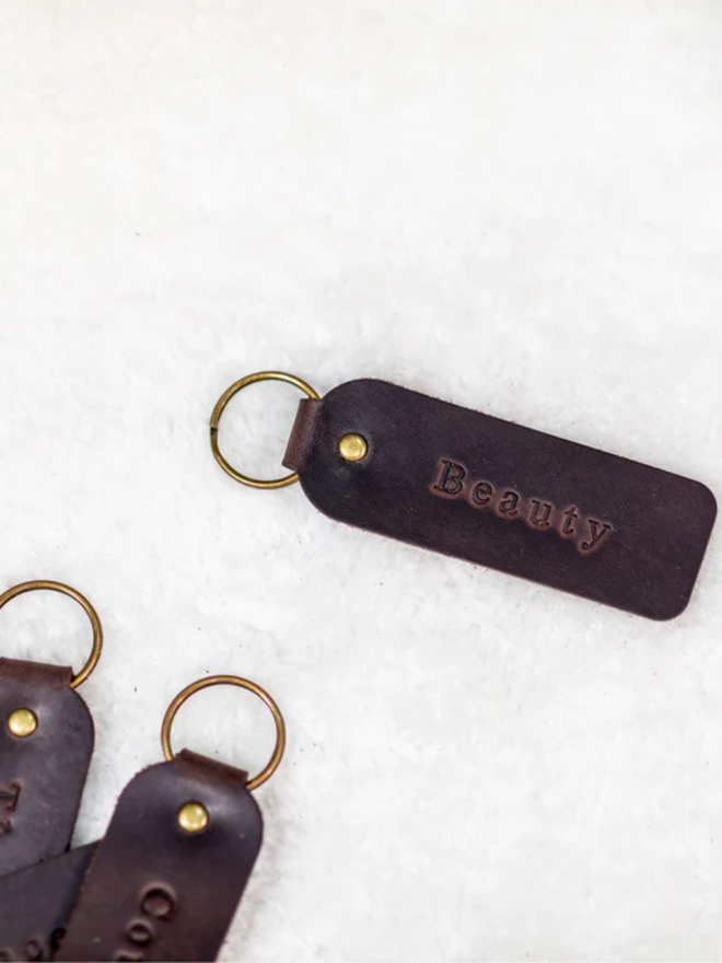 custom leather embossed keyring. a dark brown leather keyring embossed with 'beauty' photographed against a white background.